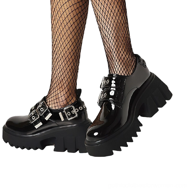 Model wearing black patent leather gothic platform loafers with fishnet stockings, low front angle showcasing shiny upper and chunky serrated platform sole