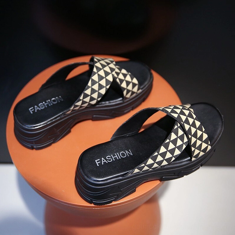 Pair of khaki and black geometric crisscross platform slides with chunky black sole, top-down overhead view on display stand