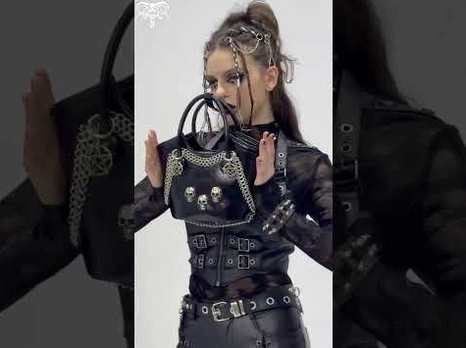 Gothic punk woman carrying black skull chain tote bag, runway-style studio photography with coordinated alternative outfit