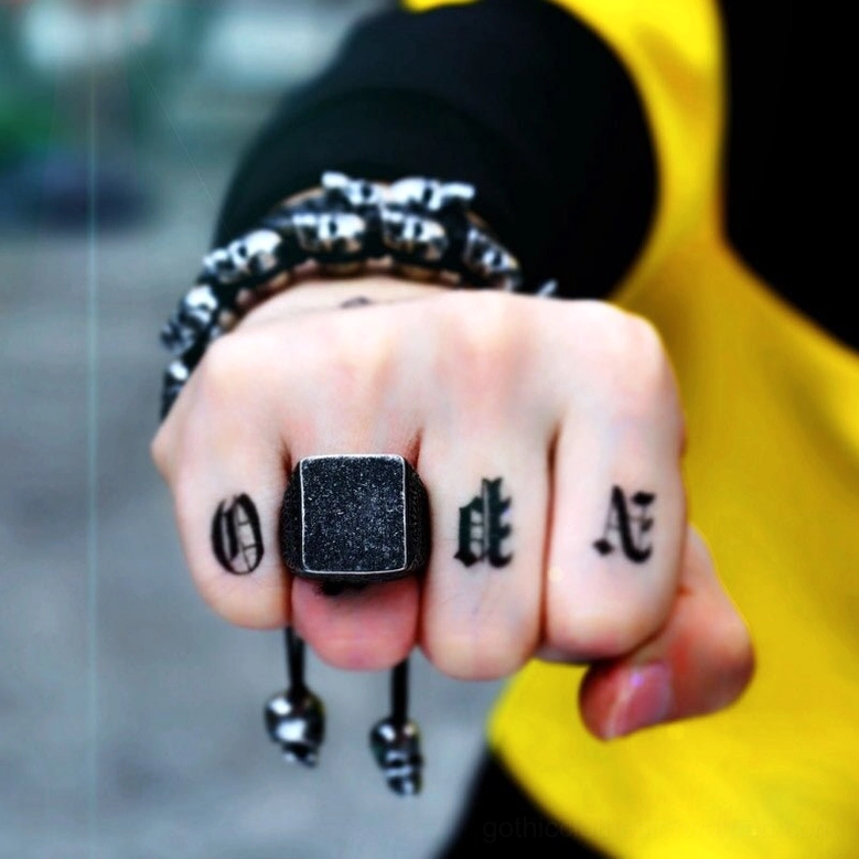 Alternative fashion statement: tattooed hand wearing dark gothic square ring paired with beaded bracelet and hanging charms outdoors