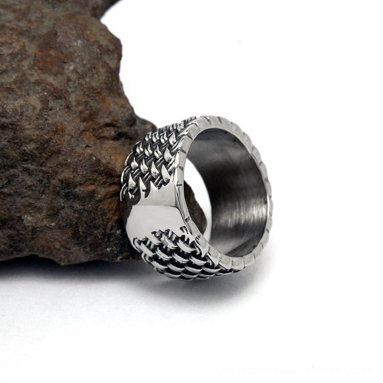 Side profile of interwoven stainless steel gothic ring on rough textured rock surface showing band depth
