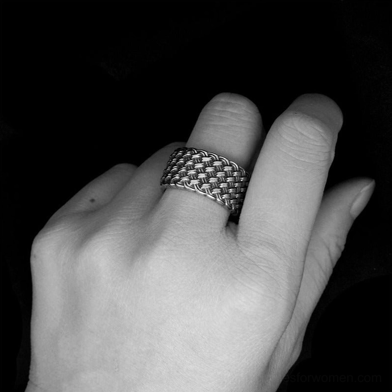 Monochrome image of interwoven gothic ring worn on female model's middle finger dark background aesthetic