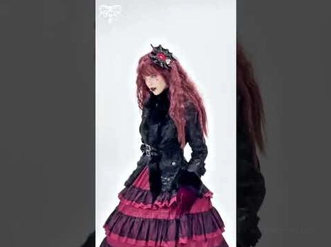 Full body styling shot of female model wearing black gothic coat with burgundy ruffled skirt and rose cross hair clip in gothic lolita ensemble