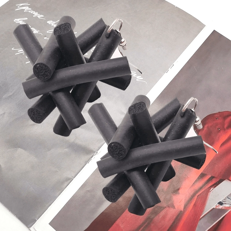 Black matte rubber drop earrings with geometric crossed-stick design on magazine page featuring goth subculture context