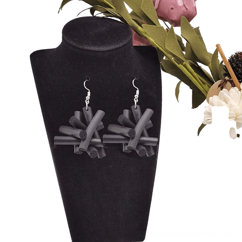 Pair of black matte rubber drop earrings displayed on black velvet jewelry stand with gothic aesthetic and decorative flowers