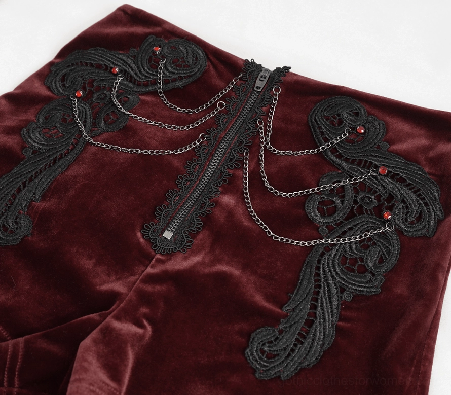 Detailed close-up of wine red velvet shorts front with black lace appliqué and decorative metal chain embellishments