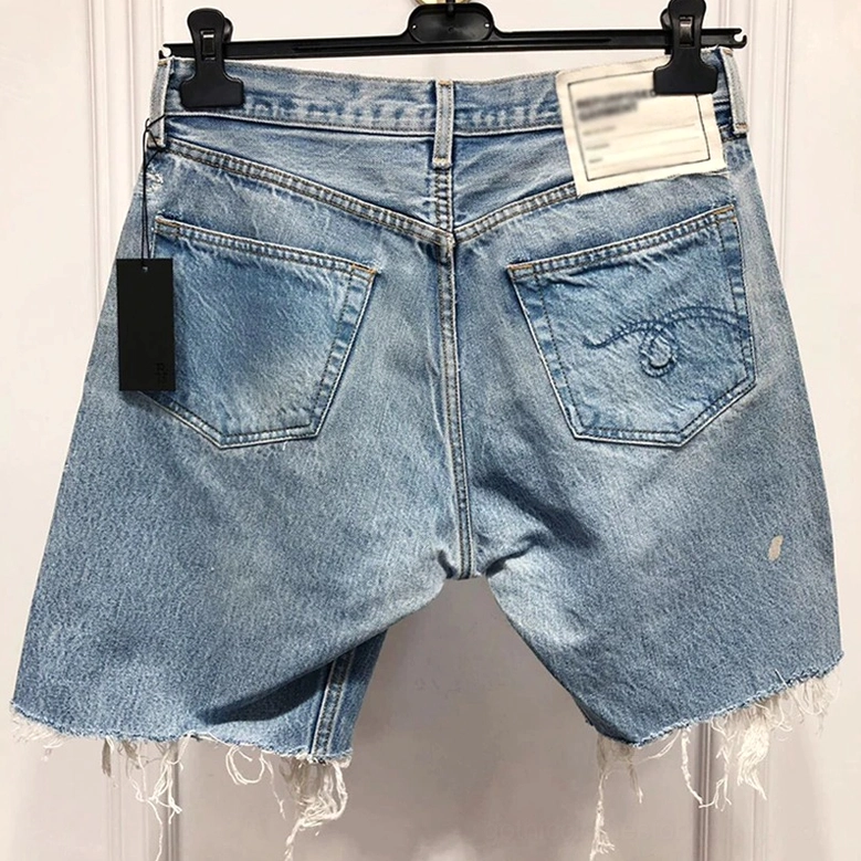Back view of light blue denim shorts on hanger showing embroidered back pockets and raw frayed hem details