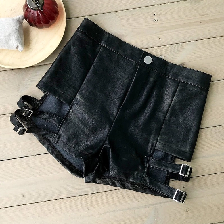 Top-down flat lay of black high-waist shorts with button closure and side buckle strap regulators