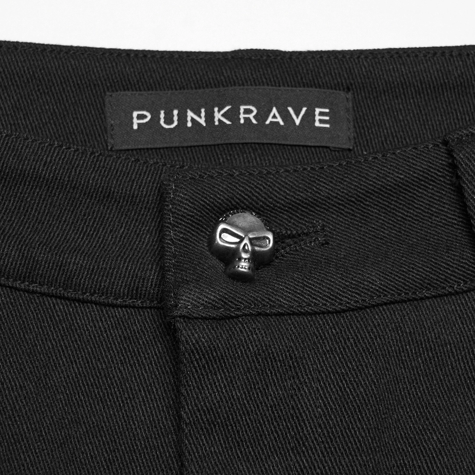 Close-up of black gothic shorts waistband with skull-shaped button fastener, PUNKRAVE branding tag, and twill fabric texture