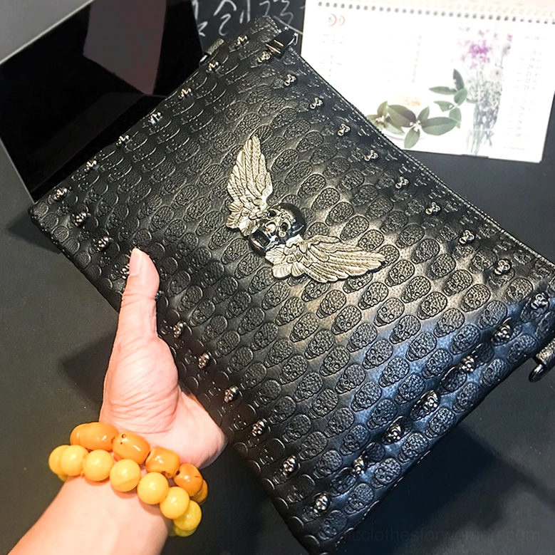 Worn gothic skull shoulder bag held by hand, displaying shape and metal wing ornament from 3/4 angle