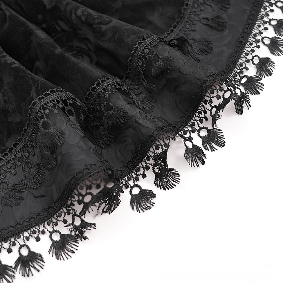 Close-up detail of black velvet gothic skirt hem showing rose embossed texture, ruffled lace tassel trim, and layered frills