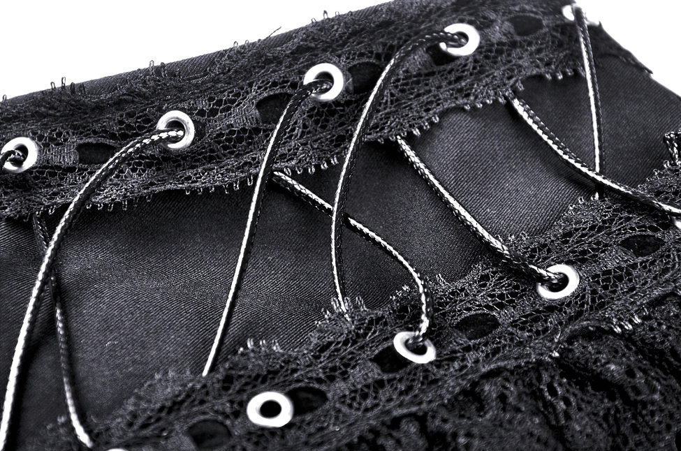 Detail shot of black gothic skirt metallic lace-up cords and embroidered lace fabric on dark background