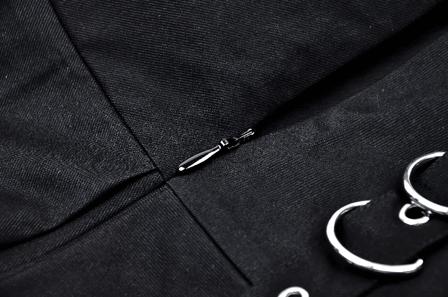 Side view close-up of black pleated gothic skirt metal O-ring straps, zipper placement, and woven fabric texture