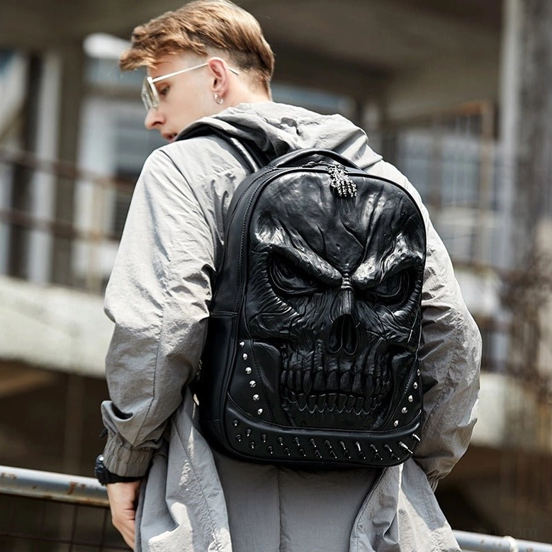 Male model wearing matte black gothic skull backpack in urban outdoor setting, street style worn back view