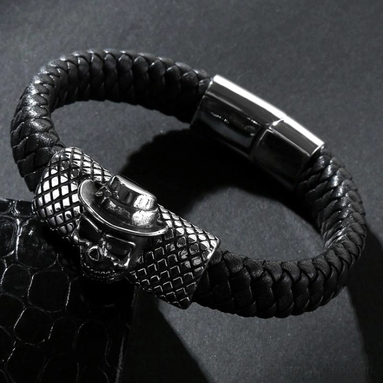 Oblique view of black leather gothic skull bracelet displaying magnetic clasp, grid-patterned metal section, fedora-topped skull detail, and braided leather texture on dark background