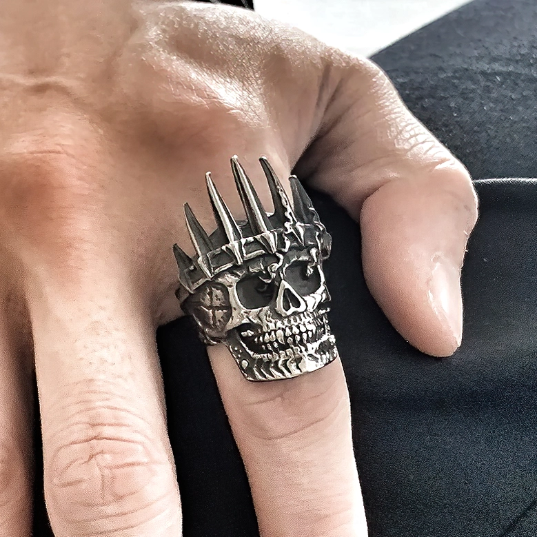 Unisex gothic skull crown ring worn on male hand index finger side view dark fabric background wearable