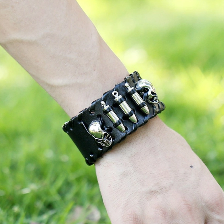 Worn on adult wrist, gothic skull leather bracelet with silver metal decor in outdoor setting, close-up side view demonstrating fit and punk aesthetic appeal