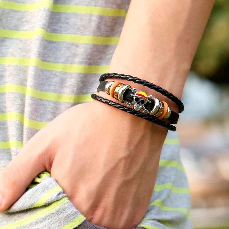 Handmade gothic skull bracelet worn on male wrist and arm, layered leather band with decorative beads, styled with casual striped clothing