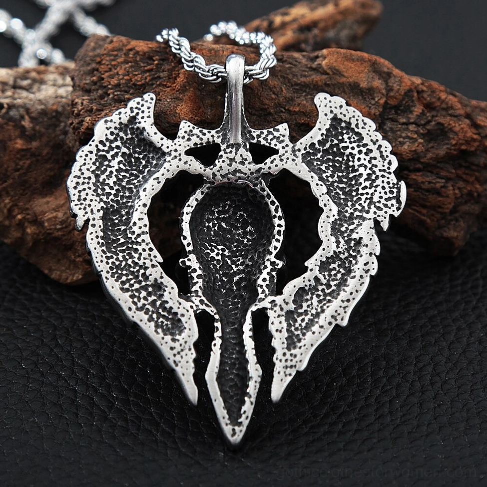 Back view of gothic winged skull pendant showing hollowed center and textured feathered wing surfaces on wood and leather mat