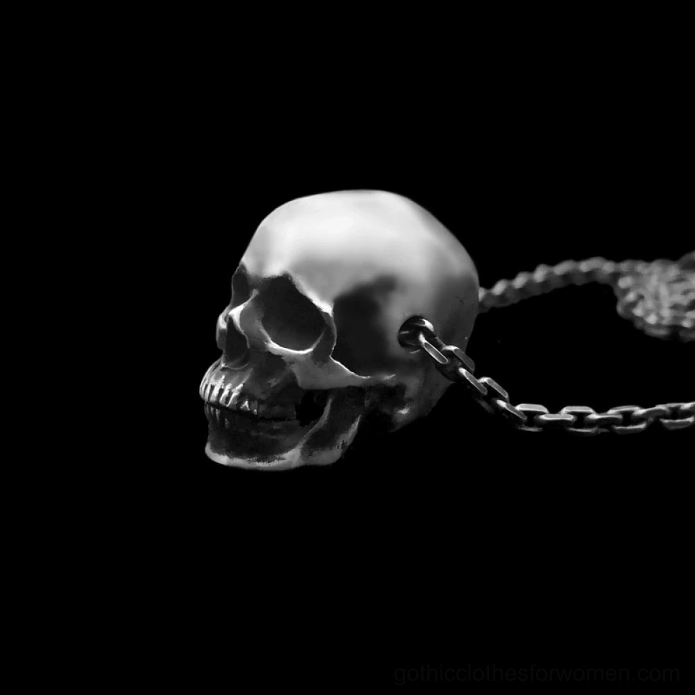 Side profile of dark metal skull pendant necklace against black background emphasizing dimensional bone structure