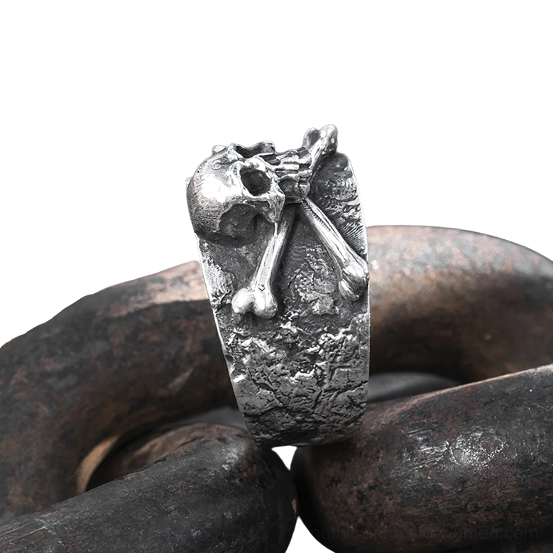 Oblique close-up of skull motif on gothic ring with rusty metal chains background, highlighting weathered sterling silver texture