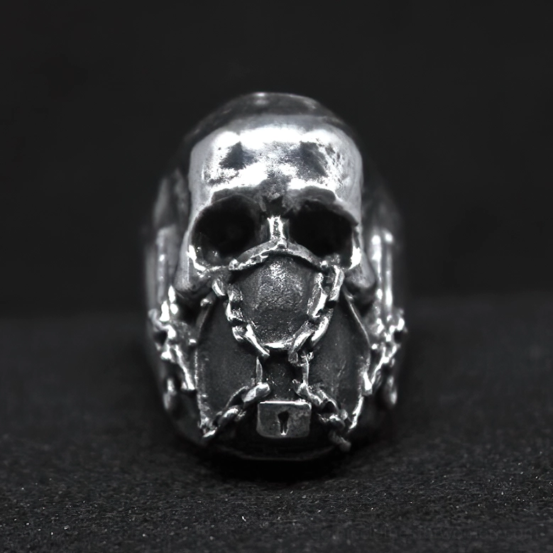 Front facing gothic skull ring with chain-wrapped mouth and lock detail on black background