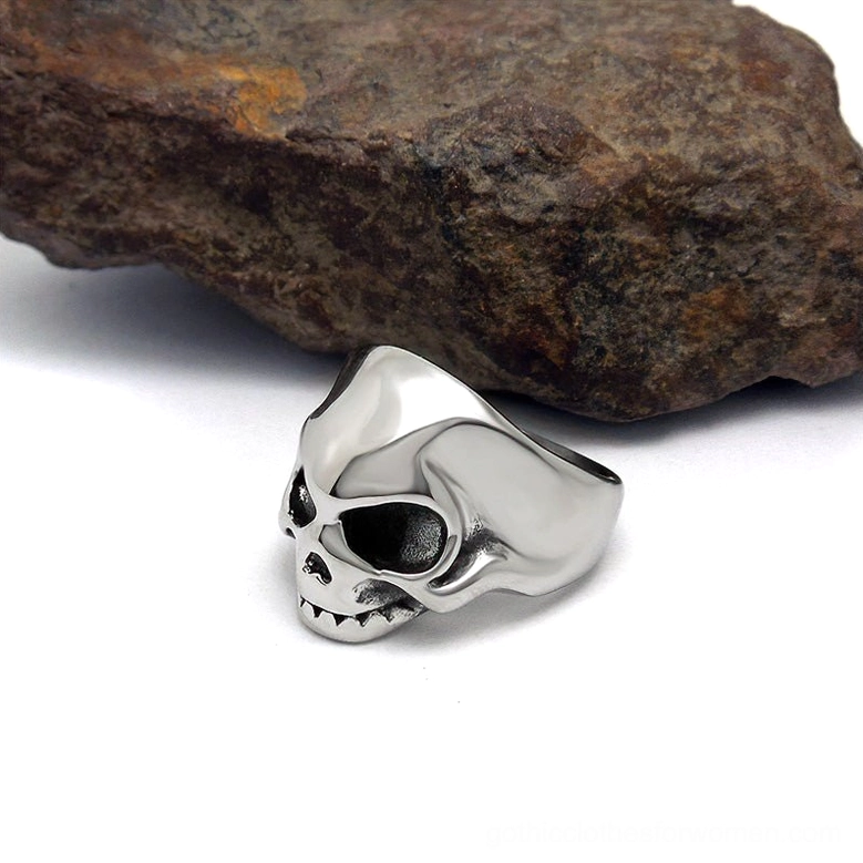 Alternative fashion skull ring left side profile view displayed against rough black rock, showing smooth polished silver stainless steel construction and simplified skull silhouette design