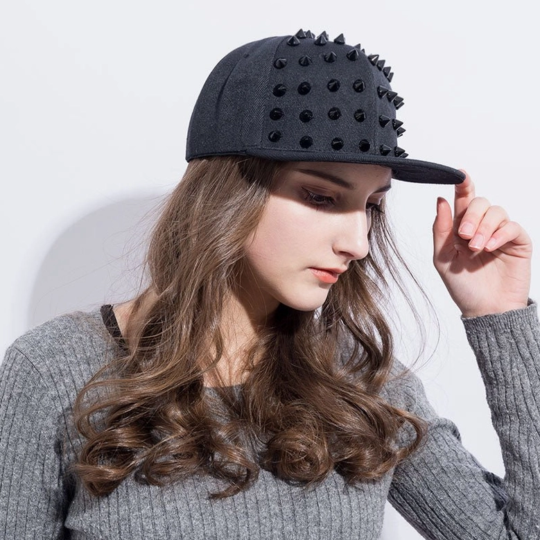 Model in right profile wearing studded punk snapback, adjusting cap brim