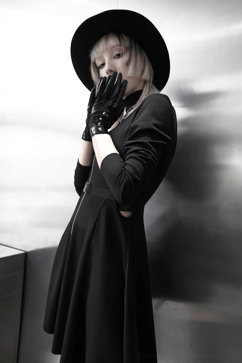 Front low-angle view of model in gothic spiked gloves covering mouth, dark alternative aesthetic, metallic background