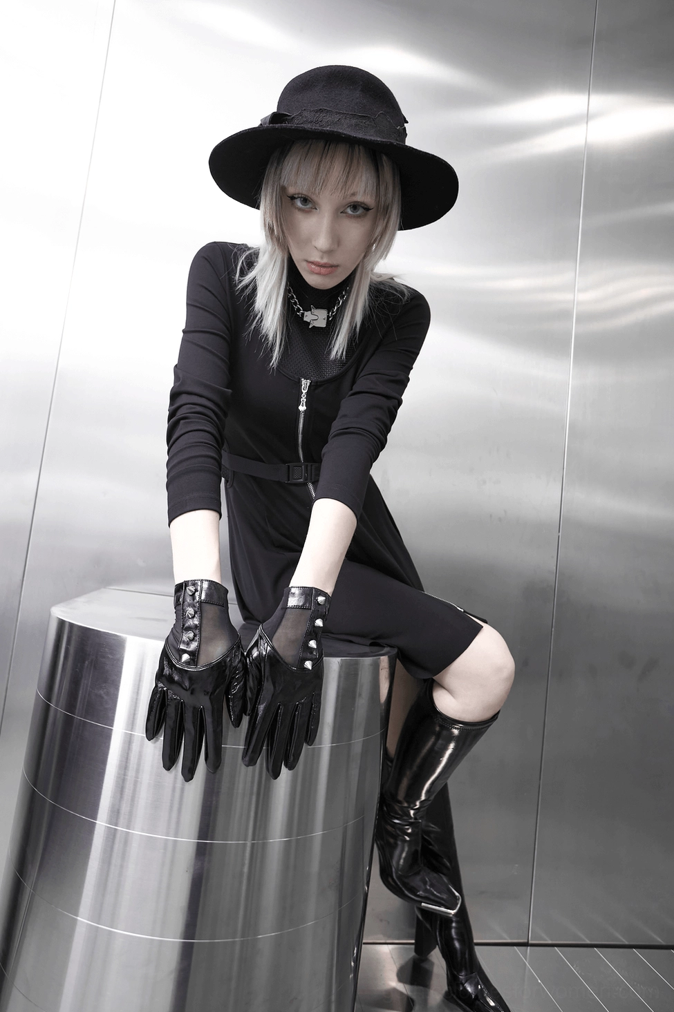 Model leaning on metal stool wearing black gothic spiked leather gloves with all-black outfit, alternative fashion