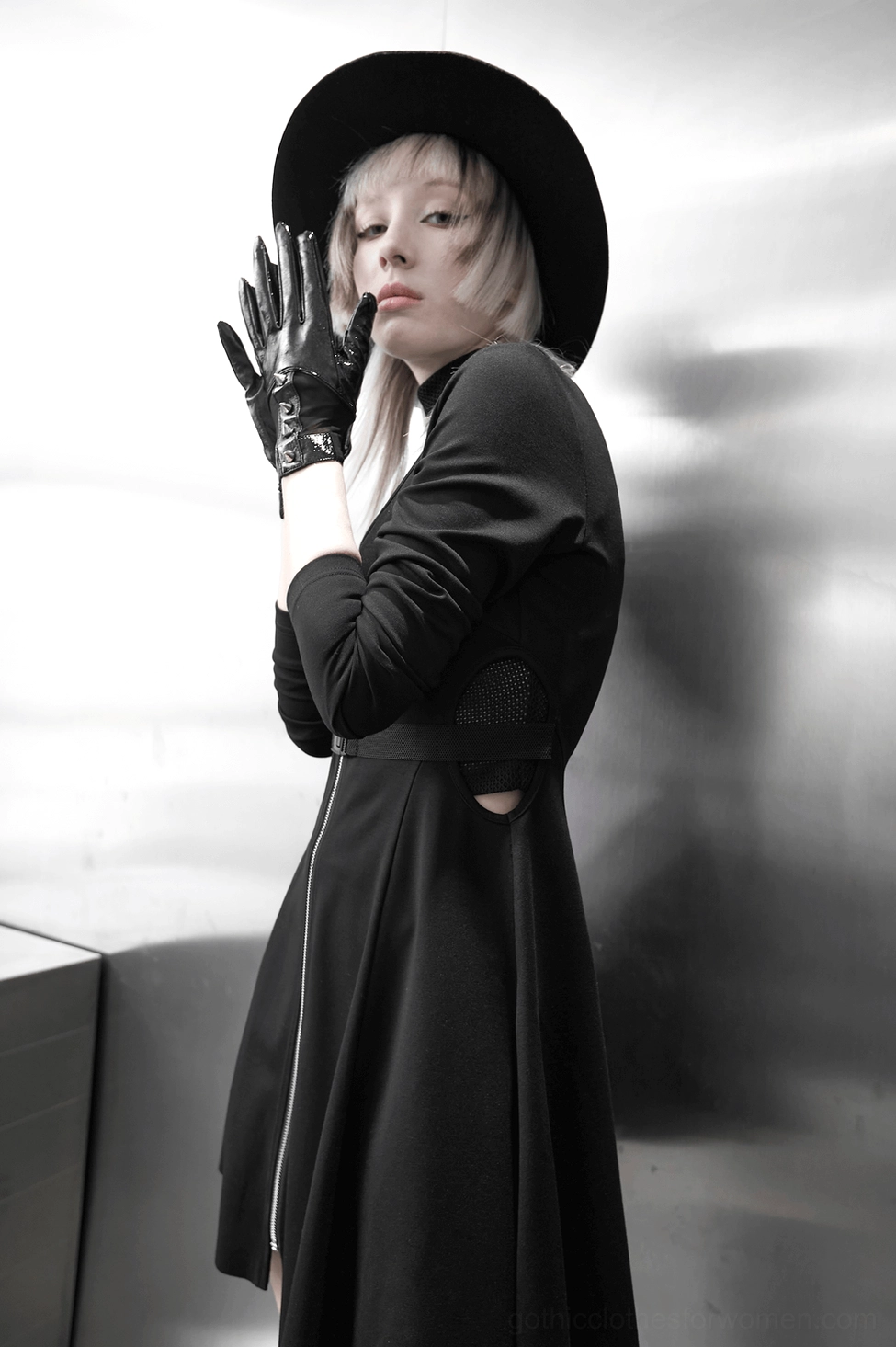 Standing side profile of model wearing black gothic spiked leather gloves with black midi dress metallic backdrop
