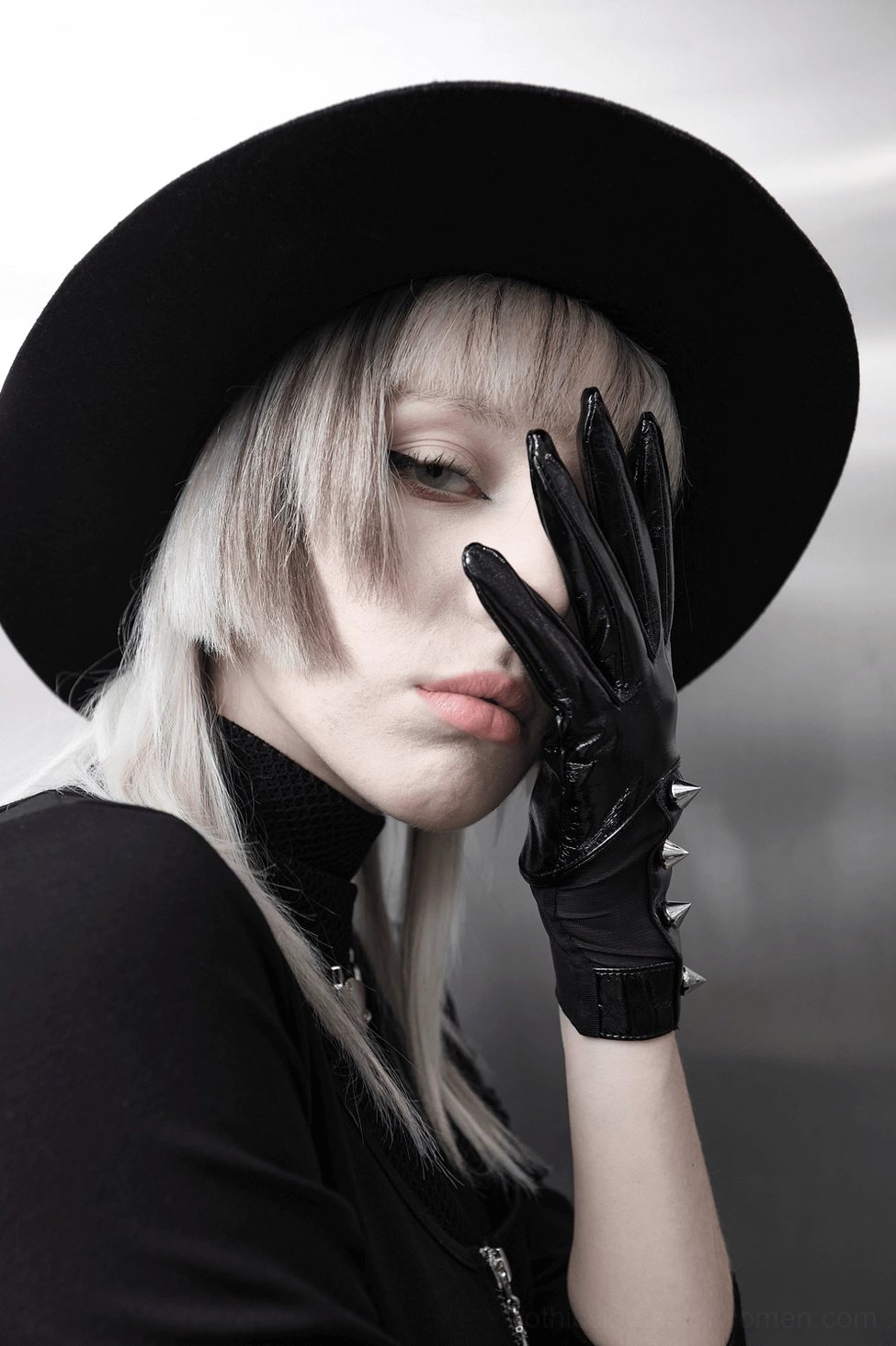Female model in wide-brim hat wearing black gothic spiked gloves with hand-on-face pose, all-black aesthetic