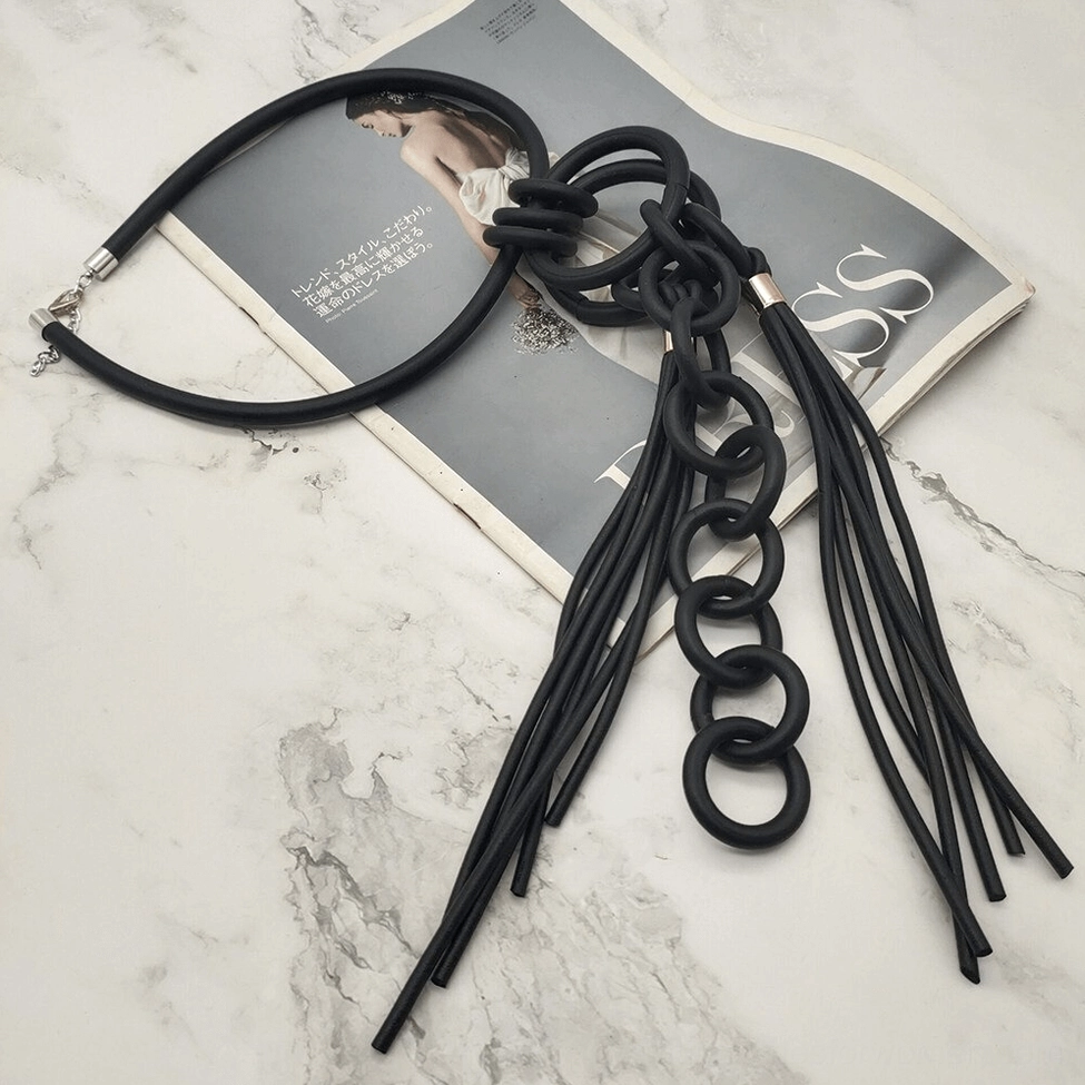 Black rubber gothic pendant necklace flat lay on marble surface with fashion magazine, showing fringe tassel and metal clasp craftsmanship