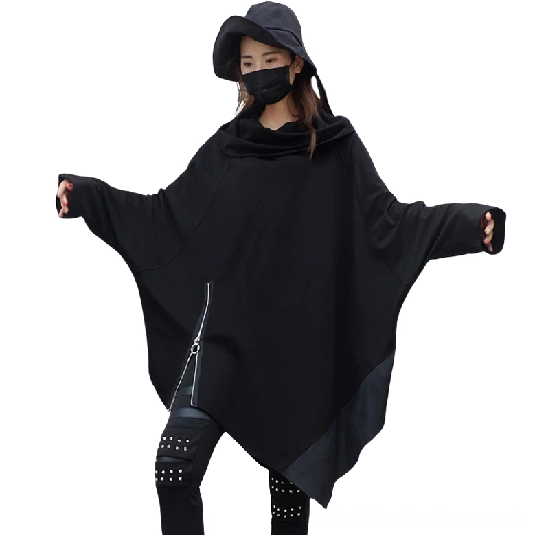 Female model wearing black asymmetrical gothic sweatshirt with batwing sleeves, studded pants and bucket hat, full-body front view