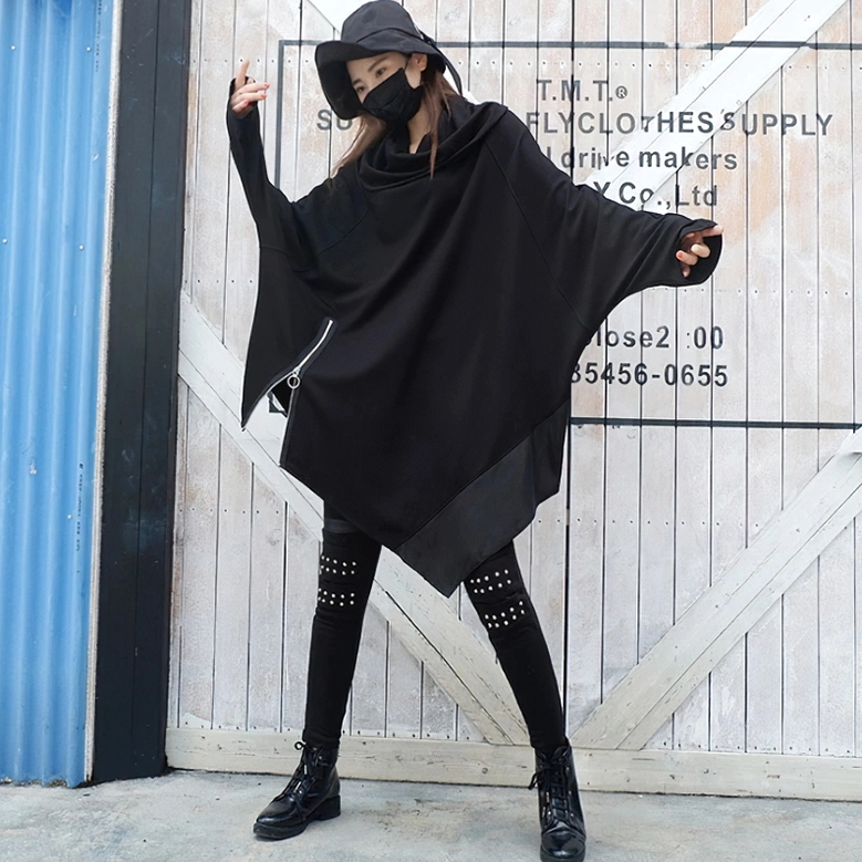 Side full-body view of model wearing asymmetrical gothic sweatshirt with combat boots on industrial wooden backdrop
