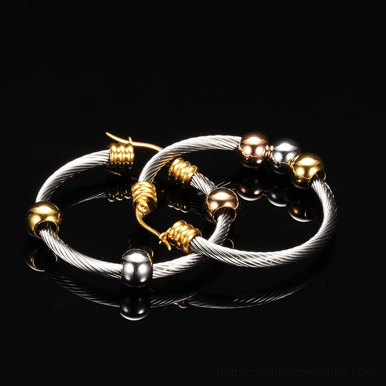 Gold hardware fastener details on twisted stainless steel gothic hoop earrings with tri-color beads on black reflective surface