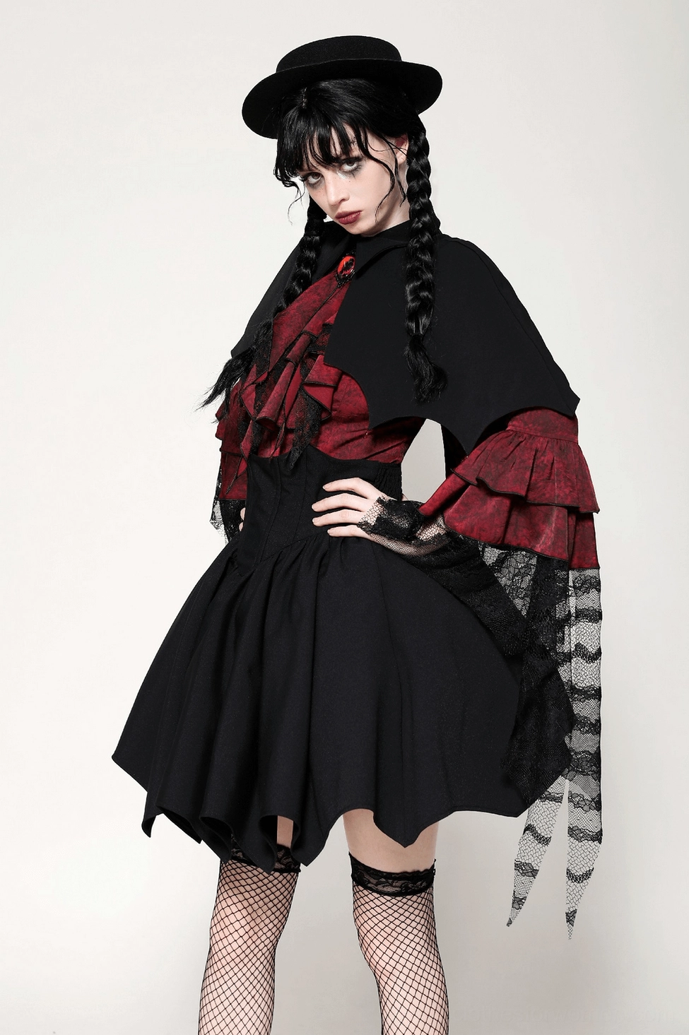 Female model wearing gothic vampire costume with cape, hand-on-hip pose, displaying fishnet stockings, ruffled lace sleeves, and irregular hem skirt