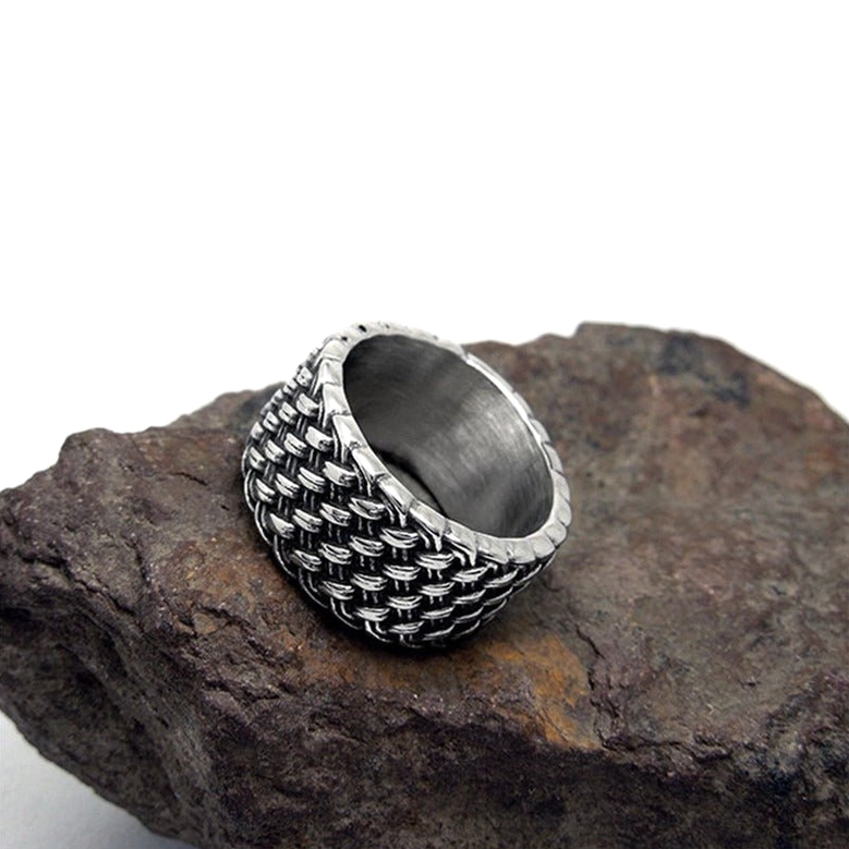 Top-down view of woven stainless steel gothic ring on rock displaying braided face design and silver tone