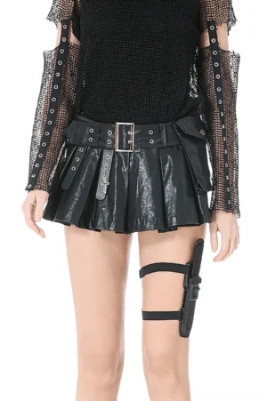 Front full-body view of high-waist pleated black faux leather skort with metal belt and cross charm, worn with thigh holster accessory