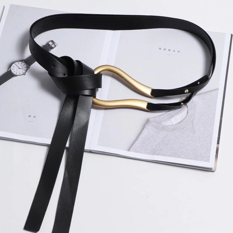 Black leather belt knotted detail flat lay on fashion magazine, gold U-shaped metal buckle and styled excess length demonstrating creative wear options