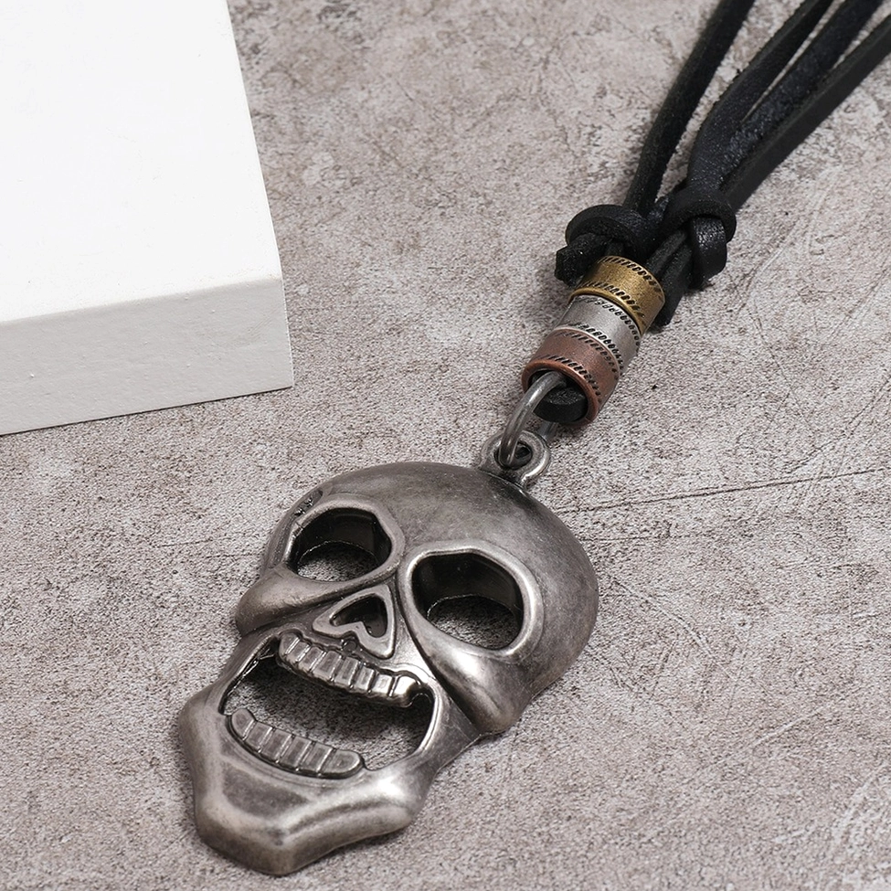 Large carved skull pendant necklace with matte silver finish, oblique angle flat lay showing teeth detail and metal work