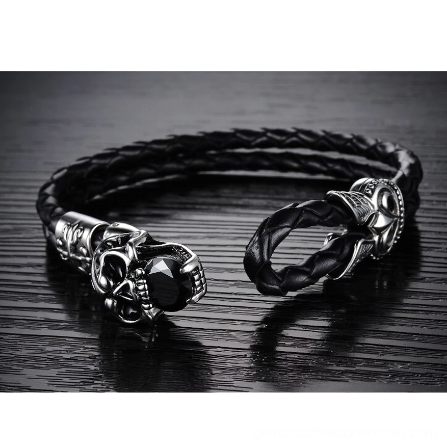 Braided black leather gothic bracelet with open buckle clasp on dark wooden surface, showing clasp mechanism