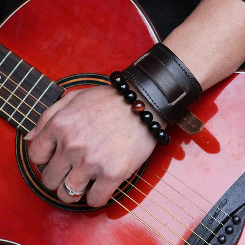 Brown leather gothic bracelet worn on male wrist beside red acoustic guitar, styled with beaded bracelets and rings, rock culture setting