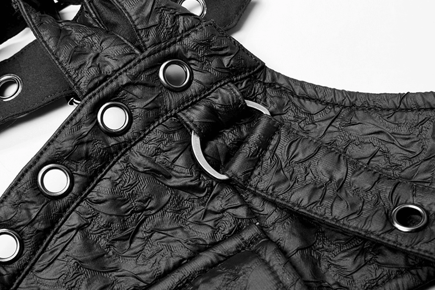 Detailed view of D-shaped metal ring, metal eyelets, and crinkled black leather strap on shoulder harness