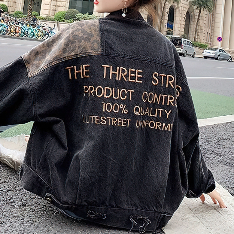 Leopard patchwork denim jacket back three-quarter view, full embroidered text visible on dark urban background