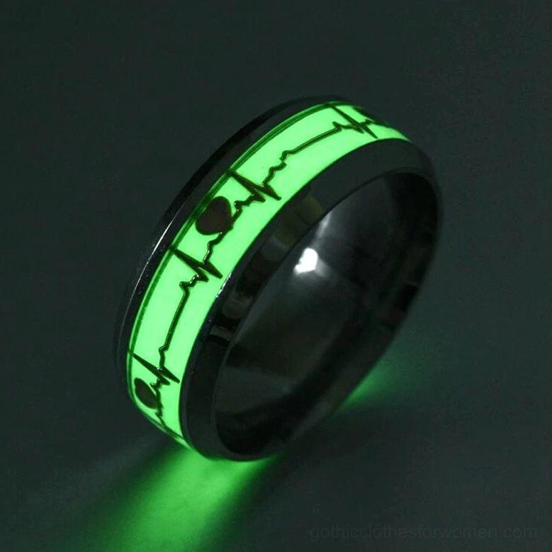 Black stainless steel luminous ECG ring, dark background close-up displaying bright green phosphorescent heartbeat band and polished frame