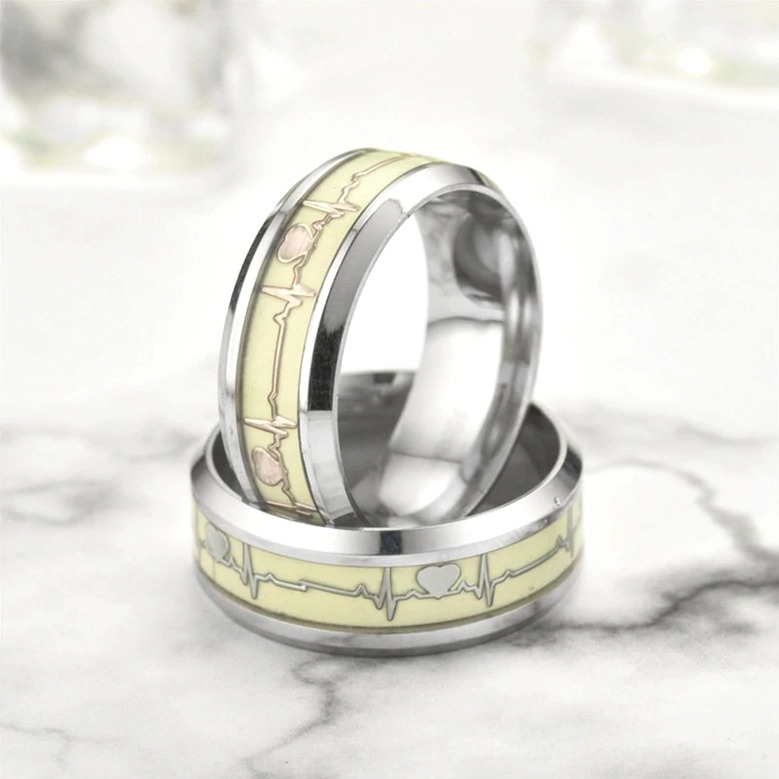 Luminous ECG heartbeat gothic rings stacked on marble surface, polished silver bands with cream glowing heart pattern and geometric ECG design