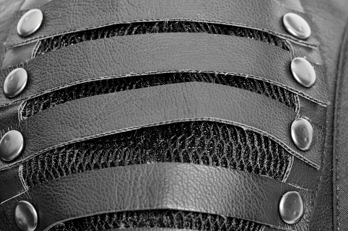 Close-up macro detail of mask front grille showing leather straps, metal rivets, and mesh underlayer construction