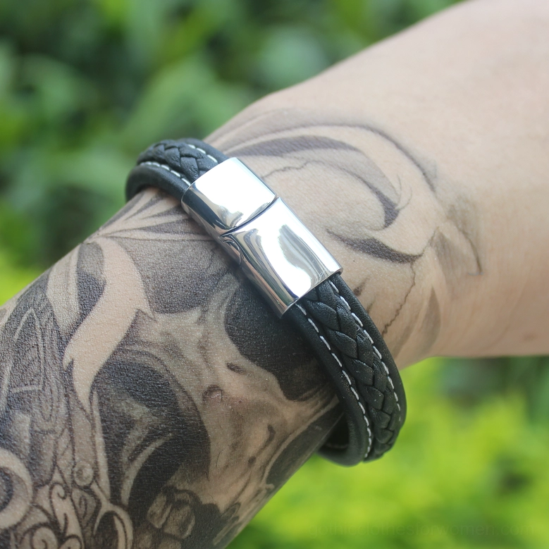 Minimalist black leather bracelet with smooth magnetic clasp on tattooed wrist, outdoor setting