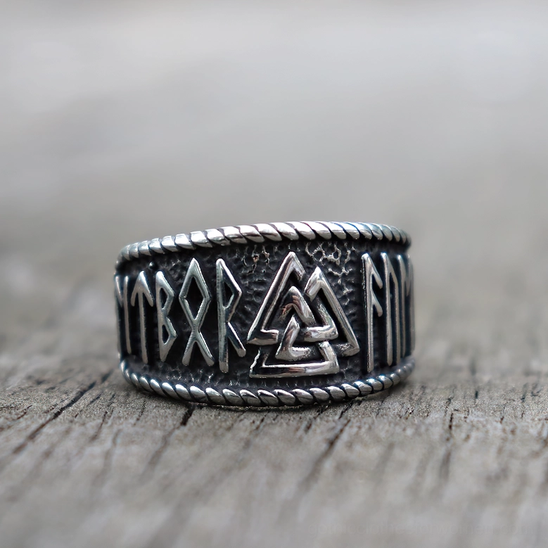 Nordic Valknut stainless steel ring flat front view displaying intricate rune carvings, twisted rope border, and textured metal finish on light wood